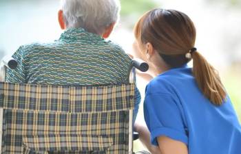 Pflegekraft spricht fürsorglich mit einem älteren Patienten im Rollstuhl